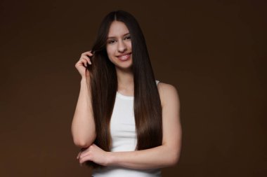 Kahverengi arka planda sağlıklı uzun saçlı gülümseyen genç kızın portresi.