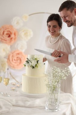 Evli çift evde bıçakla düğün pastası kesiyor, seçici bir odak noktası var.