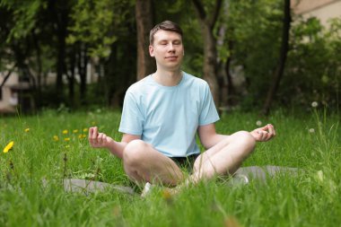 Genç adam parkta yoga yapıyor.