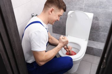 Tesisatçı içeride pompayla tuvaletin tıkanmasını açıyor.