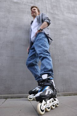 Gri duvarın yanında patenli mutlu genç adam, alçak açılı manzara.