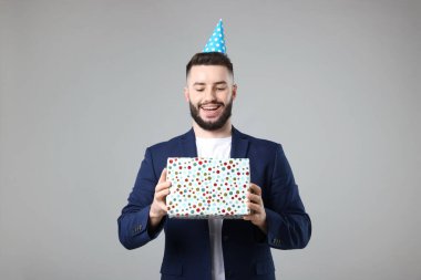 Doğum günün kutlu olsun. Gri arka planda parti şapkası ve hediye kutusu olan yakışıklı bir adam.