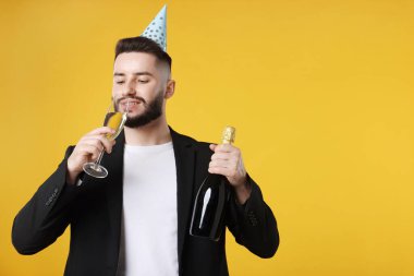 Doğum günün kutlu olsun. Turuncu arka planda parti şapkası ve şampanyası olan yakışıklı bir adam.