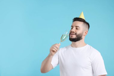 Doğum günün kutlu olsun. Açık mavi arka planda parti şapkası ve bir bardak şampanyası olan yakışıklı bir adam.
