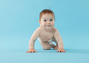 Açık mavi arka planda emekleyen şirin bir bebek.