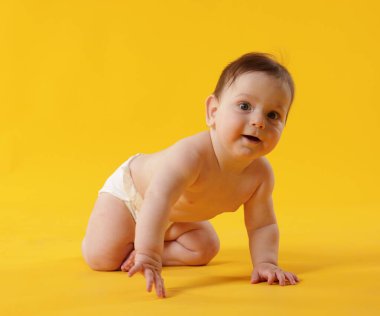 Sarı arka planda emekleyen sevimli küçük bebek.