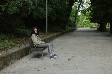 Evsiz kadın parkta bankta oturuyor, mesaj için yer var.