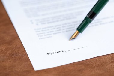 Kahverengi deri yüzeyinde dolma kalemle noter belgesi imzalanırken, yakın plan