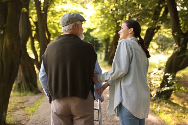 Gülümseyen bakıcı dışarıda yürüyen çerçeve kullanan yaşlı adamı destekliyor.