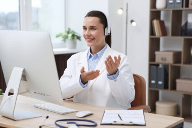 Kulaklıklı doktor klinikteki bilgisayar aracılığıyla online danışmanlık yapıyor.