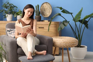 Uyum. Evdeki yeşil bitkiler arasında koltukta kitap okuyan güzel bir kadın.