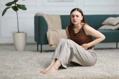 Karın ağrısı çeken bir kadın evinde yerde yatıyor, mesaj için yer var.