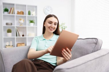 Evdeki koltukta modern tablet kullanan genç bir kadın.