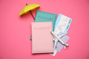 Uçak modeli, pasaportlar, uçuş biletleri, kredi kartı ve pembe arka planda küçük şemsiye, düz konum