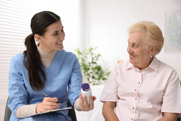 Nurse giving pills to senior woman indoors. Home health care service
