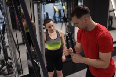 Profesyonel özel antrenör, genç bayana spor salonunda spor aletini nasıl kullanacağını gösteriyor.