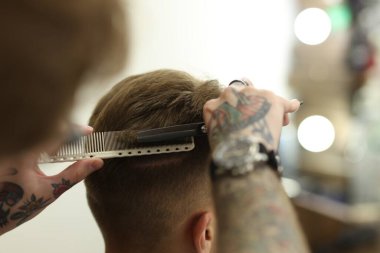 Profesyonel berber, berber dükkanında müşterinin saçını makasla kesiyor.
