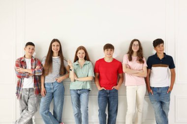 Beyaz duvarın yanında poz veren bir grup mutlu genç.