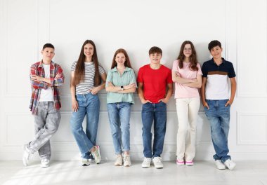 Beyaz duvarın yanında poz veren bir grup mutlu genç.