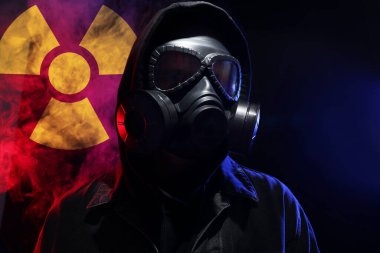 Siyah arka planda duman içinde gaz maskesi takan adam. Arkasında radyoaktif bir işaret var.