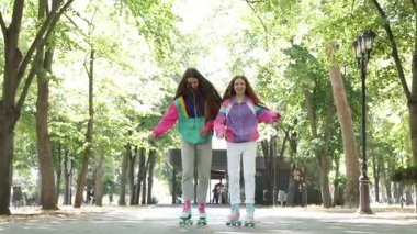 İki genç kız şehir caddesinde birlikte paten kayıyor.