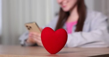 Online flört sitesi. İçerideki masada akıllı telefon kullanan kadın dekoratif kalbe odaklan.