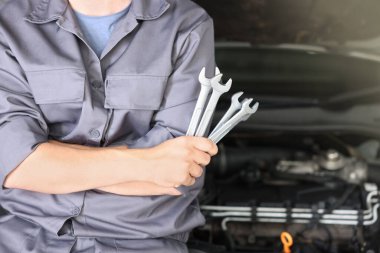 Otomobil parçaları. Kaputu açık, kapalı kaputun yanında anahtarı olan profesyonel bir tamirci, yakın plan. Metin için boşluk