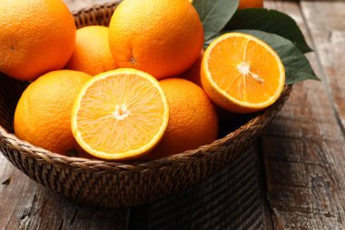 Taze portakallar ve yapraklar hasır sepetin içinde ahşap masanın üzerinde, yakın plan.