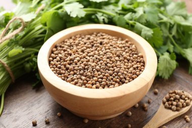 Taze kişniş ve kişniş tohumları ahşap masada, yakın plan.