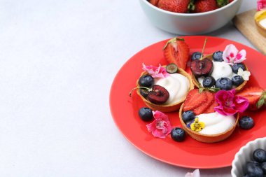 Açık gri masada böğürtlenli ve çiçekli tatlı tartlar, yazı için yeri olan yakın plan. Tatlı nefis.