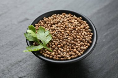 Kişniş tohumu ve taze kişniş yaprakları koyu dokulu masada, yakın plan.