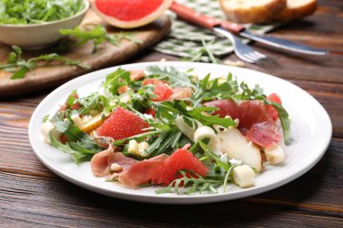 Lezzetli salata roka, prosciutto, peynir, armut, greyfurt ve ahşap masada fındık, yakın plan.