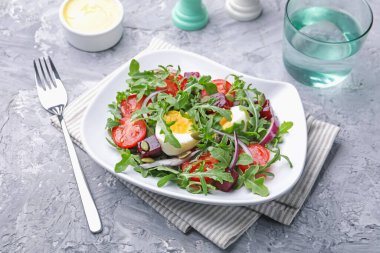 Lezzetli salata roka, sebze ve yumurta gri masada servis edilir, yakın plan.