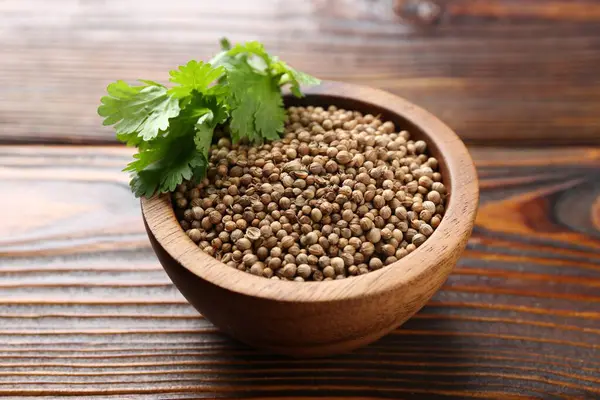 Kişniş tohumu ve taze kişniş yaprakları ahşap masada, yakın plan.