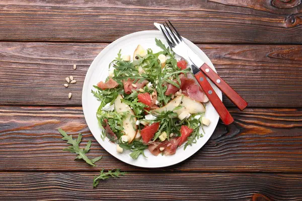 Lezzetli salata roka, prosciutto, peynir, armut, greyfurt ve fındıklar ahşap masanın üstünde.