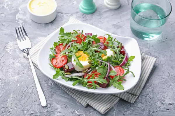 Lezzetli salata roka, sebze ve yumurta gri masada servis edilir, yakın plan.