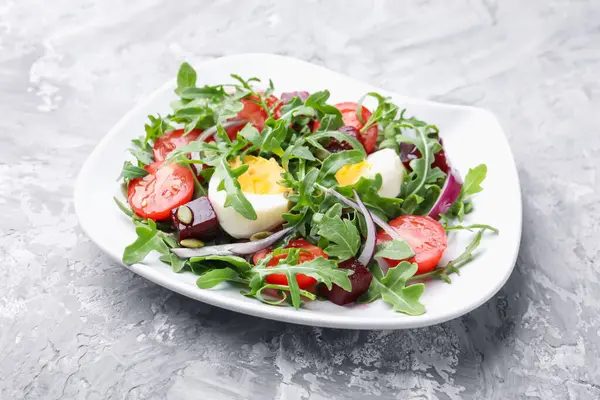 Lezzetli salata roka, sebze, yumurta ve tohumlar gri masada, yakın plan.