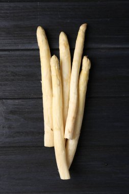 Siyah ahşap masada çiğ beyaz kuşkonmaz mızrakları.