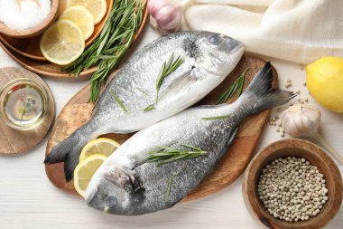 Taze çiğ dorado balığı, limon dilimleri, biberiye ve baharatlar beyaz ahşap masa, düz yatak. Organik deniz ürünleri