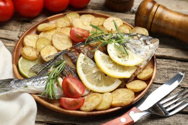 Ahşap masada patates, domates ve limonla servis edilen kızarmış dorado balığı. Ev yapımı deniz ürünleri yemeği.