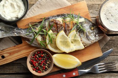 Ahşap masada biberiye ve limonla servis edilen kızarmış dorado balığı. Ev yapımı deniz ürünleri yemeği.