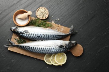 Deniz ürünleri lezzetleri. Taze çiğ uskumrular ve baharatlar siyah masada, düz yerde. Metin için boşluk