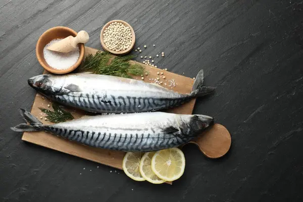Deniz ürünleri lezzetleri. Taze çiğ uskumrular ve baharatlar siyah masada, düz yerde. Metin için boşluk