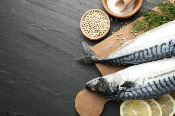 Deniz ürünleri lezzetleri. Taze çiğ uskumrular ve baharatlar siyah masada, düz yerde. Metin için boşluk