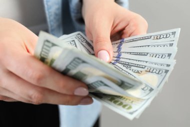 Açık gri arka planda dolar banknotları sayan kadın, yakın plan