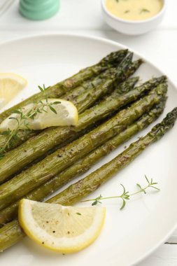 Beyaz ahşap masada limon ve kekik ile servis edilen lezzetli pişmiş kuşkonmaz, yakın plan.