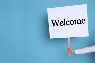 Açık mavi arka planda hoş geldin tabelası tutan kadın, yakın plan