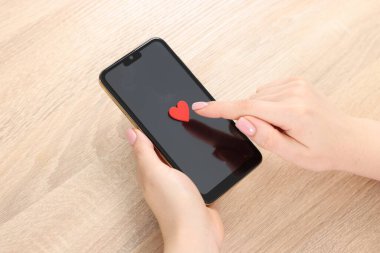 Online flört sitesi. Ahşap masadaki akıllı telefonda kırmızı kalbe dokunan kadın.