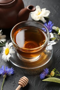 Cam bardakta Aromatik bitki çayı, farklı çiçekler ve siyah masada çaydanlık, yakın plan.