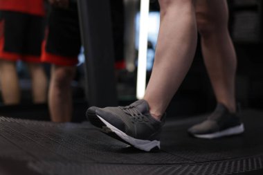 Spor salonunda profesyonel antrenörle koşu bandında egzersiz yapan genç bir kadın.